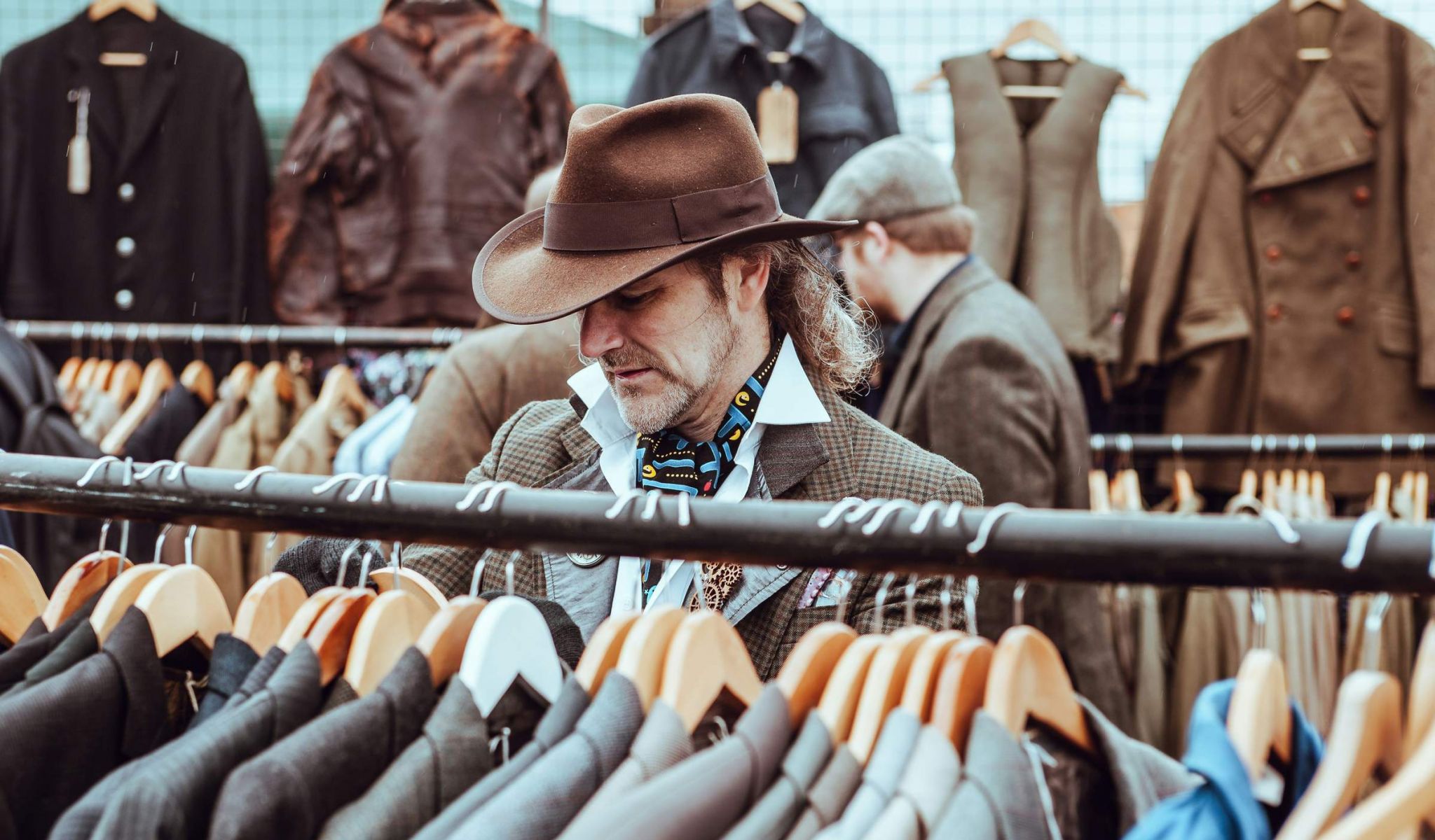 Man shopping in a retail store lookin at suit coats while wearing a top hat