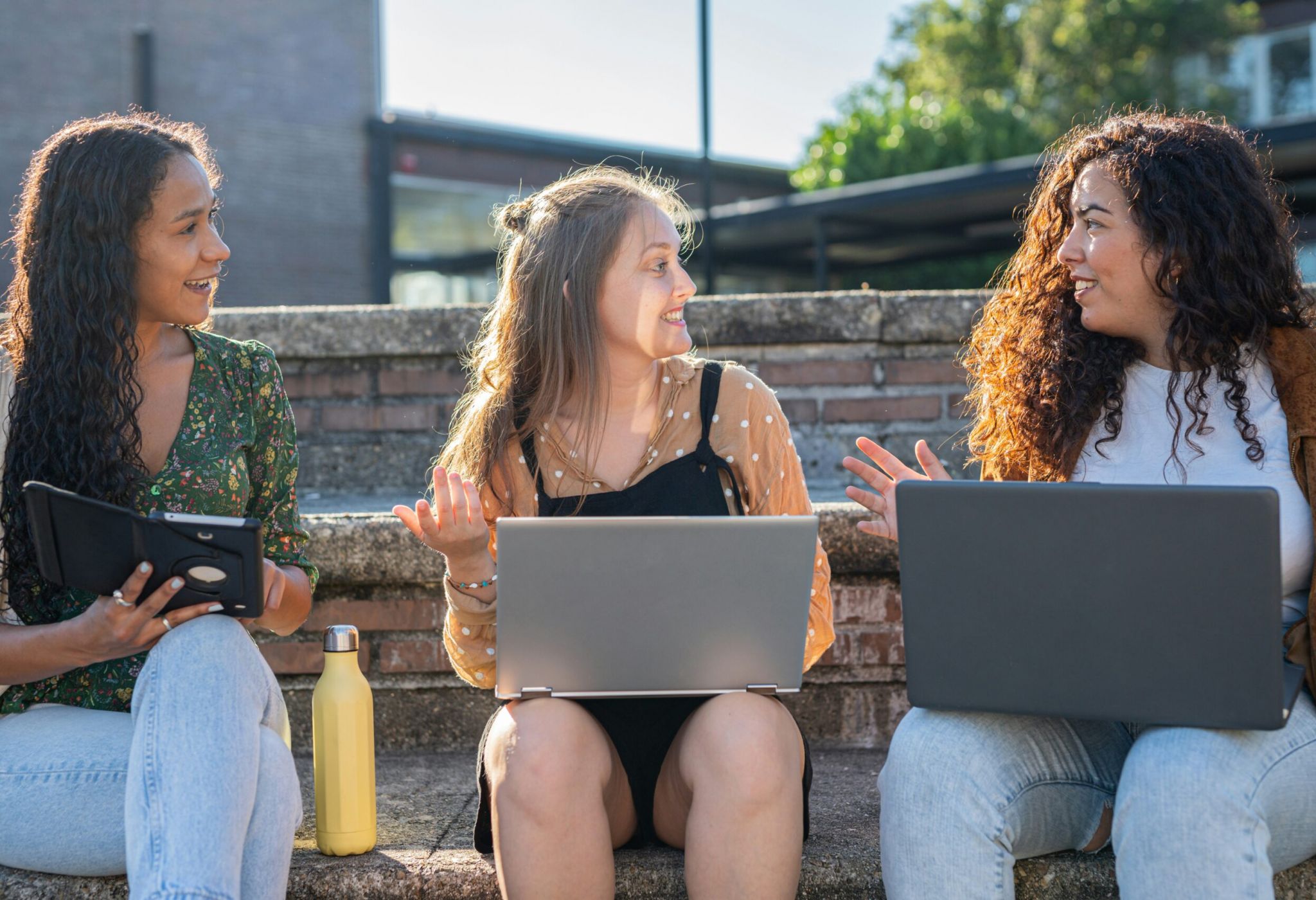 Girls at UNC Chapel Hill sitting on steps with computers on their laps looking for apartments