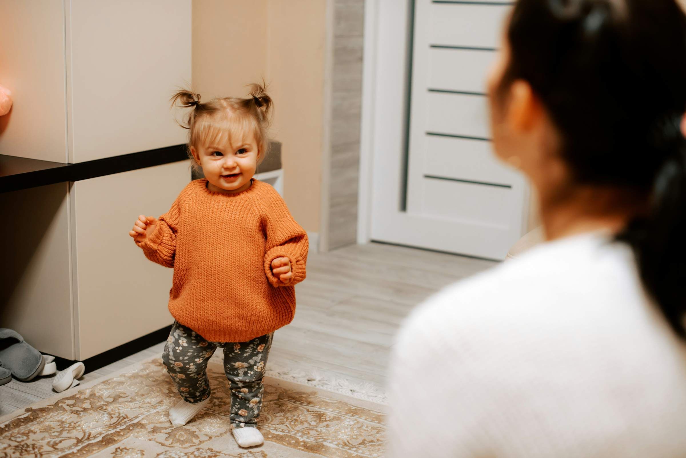 toddler wearing a orange sweater smiling at her mom who is out of the frame