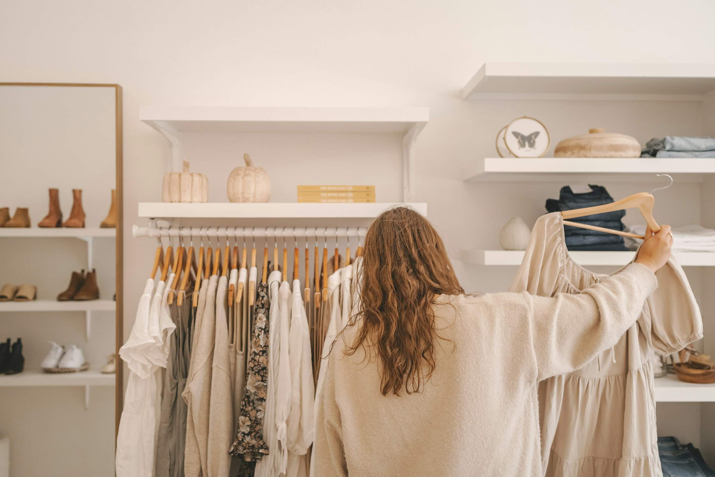 Woman wearing beige shirt shopping for another beige shirt in a store with lots of beige tones